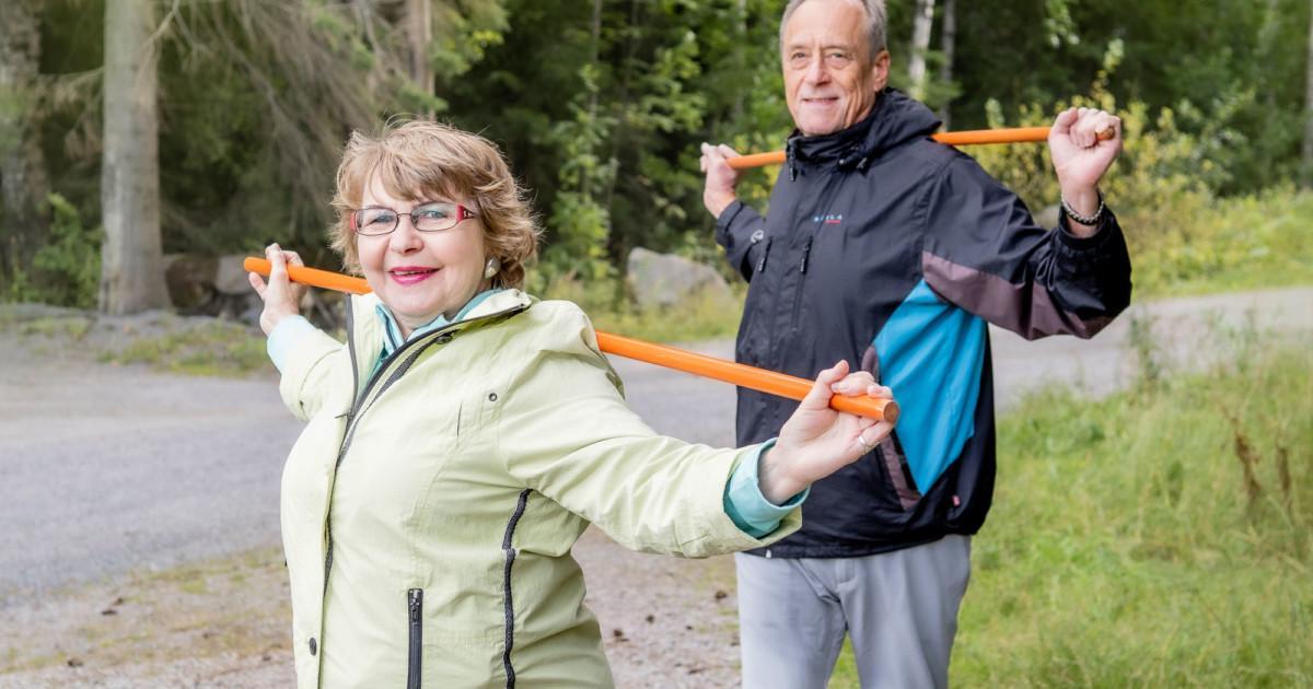 Iäkäs pariskunta jumppaa keppien kanssa kuntoradalla.