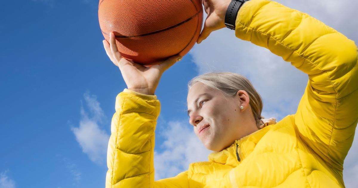 Keltaiseen takkiin pukeutunut tyttö heittää koripalloa ulkona.