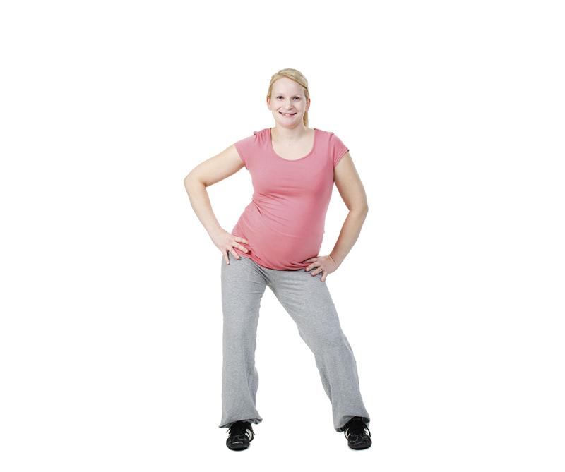 A pregnant woman is doing a hip swing exercise.