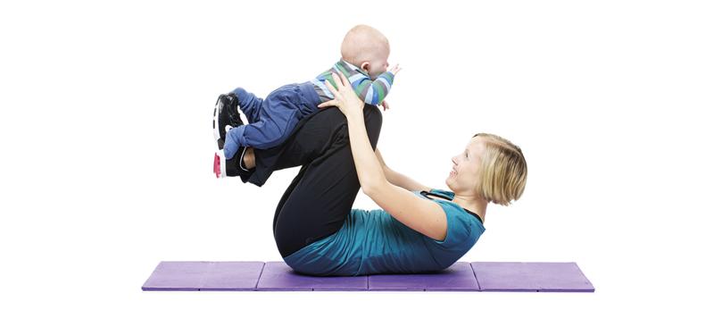 A woman is doing holding her baby on her shins while lying on the mat.