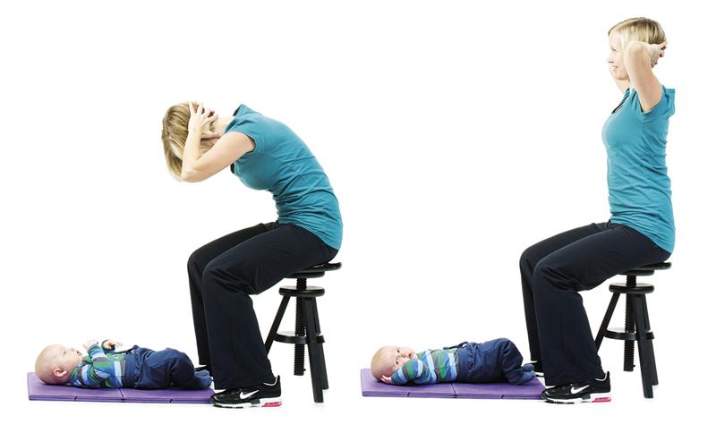 A woman is sitting on a chair and rounding her back while her baby is lying on the mat.