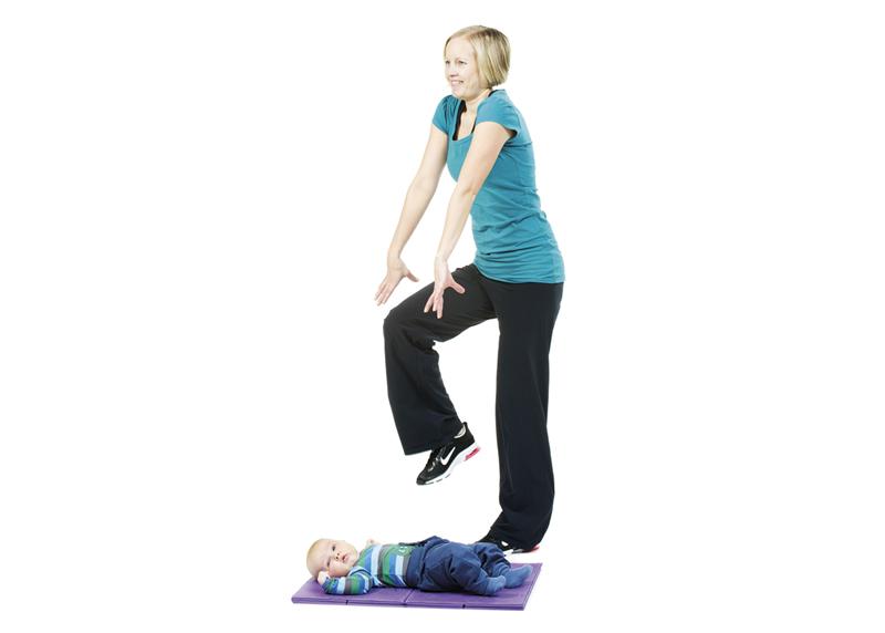 A woman is marching in place and rotating shoulders while her baby is lying on the mat.