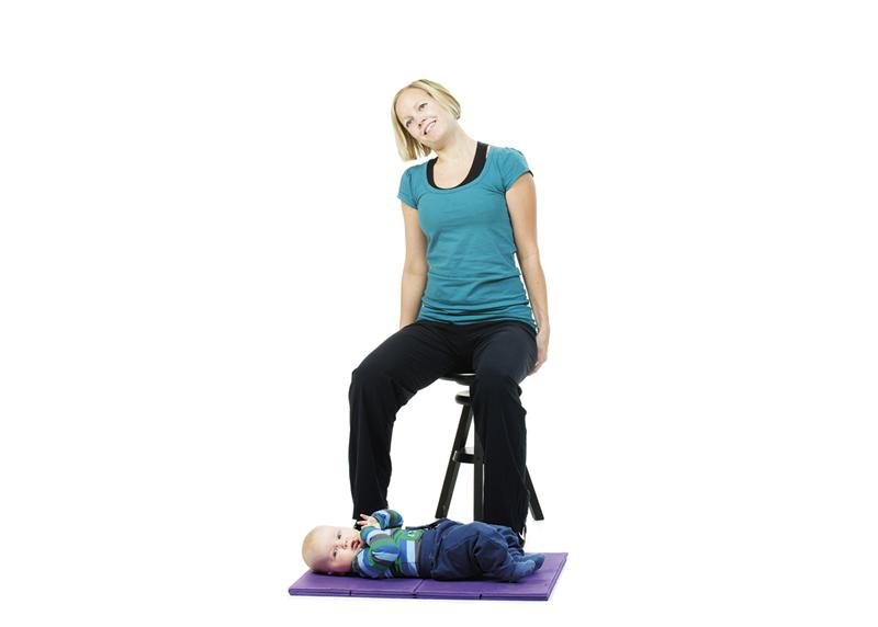 A woman is sitting on a chair and stretching her neck while her baby is lying