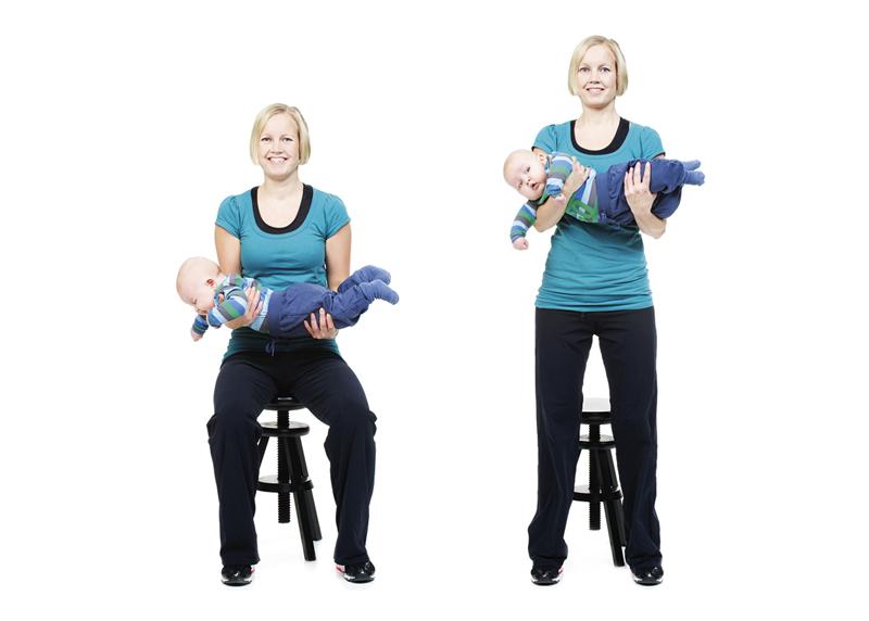 A woman is doing squats while holding her baby on forearms.
