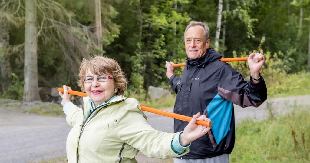 En man och en kvinna med gymnastikstavar på axlarna vid skogsbrynet.